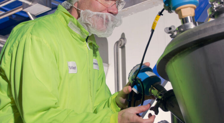 Technician in hi-vis and hairnet checking equipment on an industrial tank
