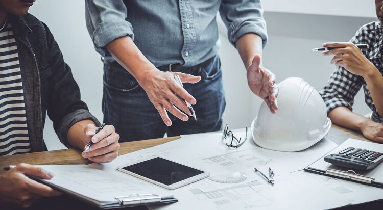 Engineers reviewing building plans with a hard hat on the table